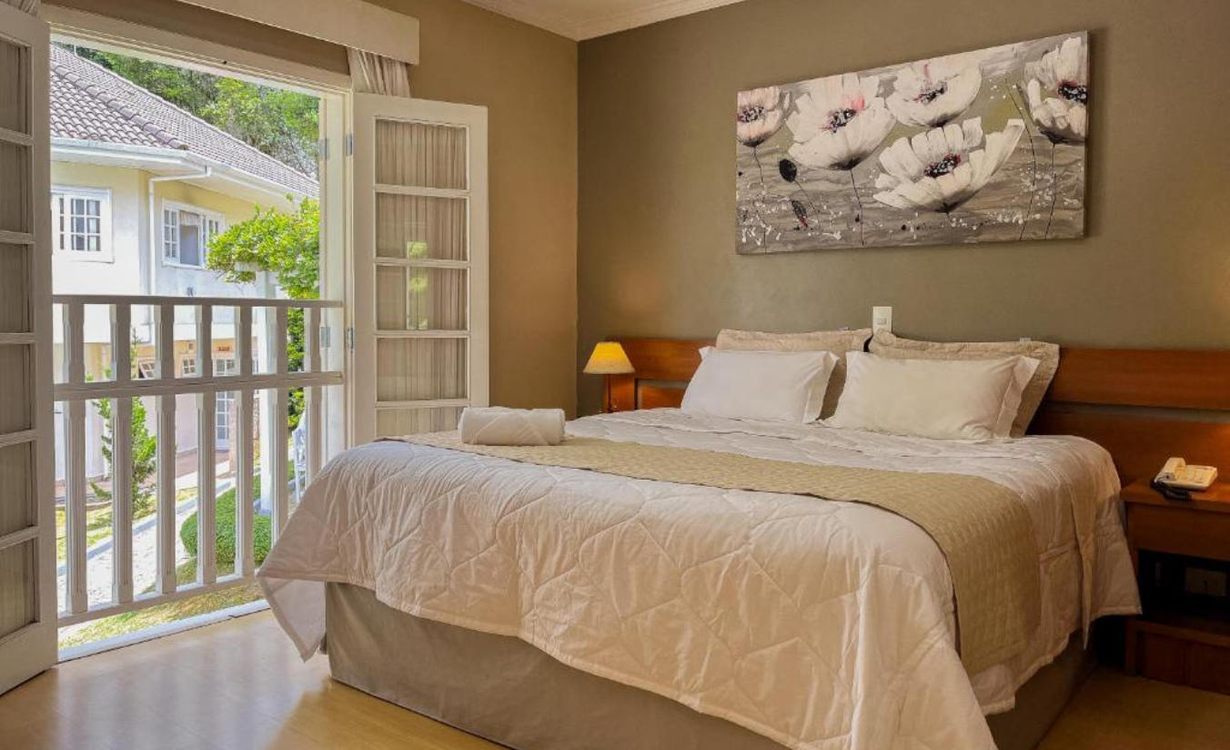 Apartamento Superior da Pousada Nacional Inn com porta-balcão aberta para o jardim e cama king size ao fundo