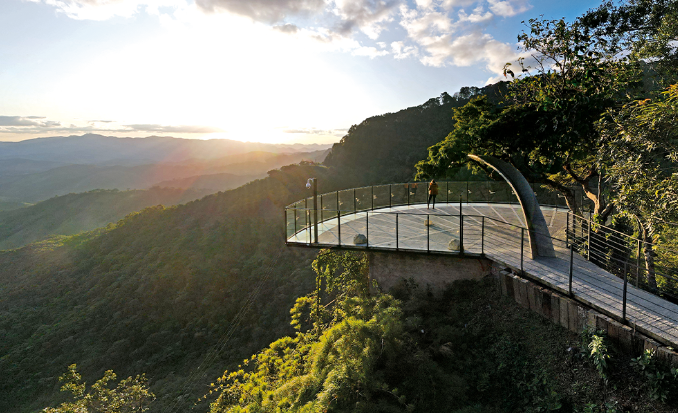 Vista panorâmica da Serra da Mantiqueira a partir do Jardim Belvedere em Campos do Jordão, com araucárias em primeiro plano e névoa nas montanhas ao amanhecer