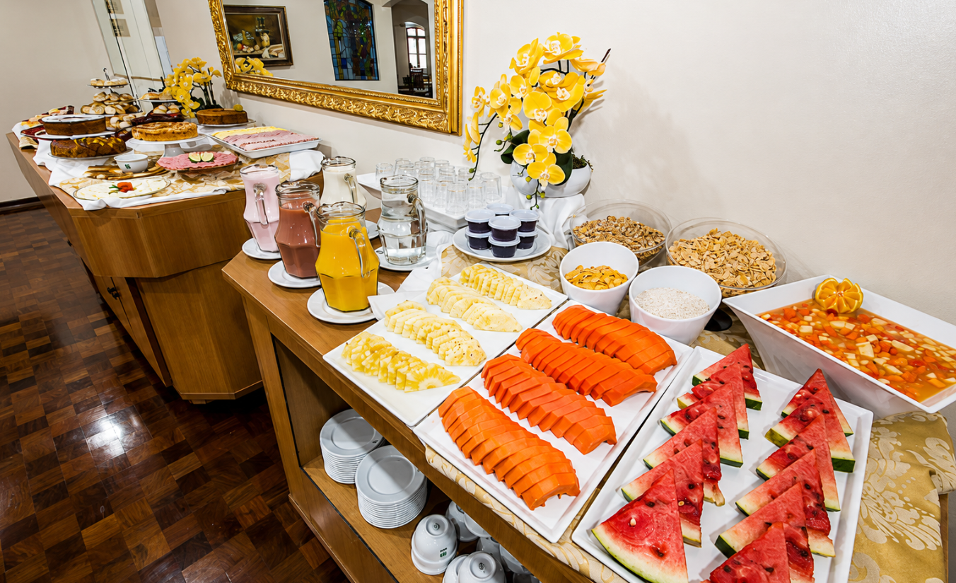 Buffet de café da manhã com pães, queijos e frutas variadas em ambiente aconchegante